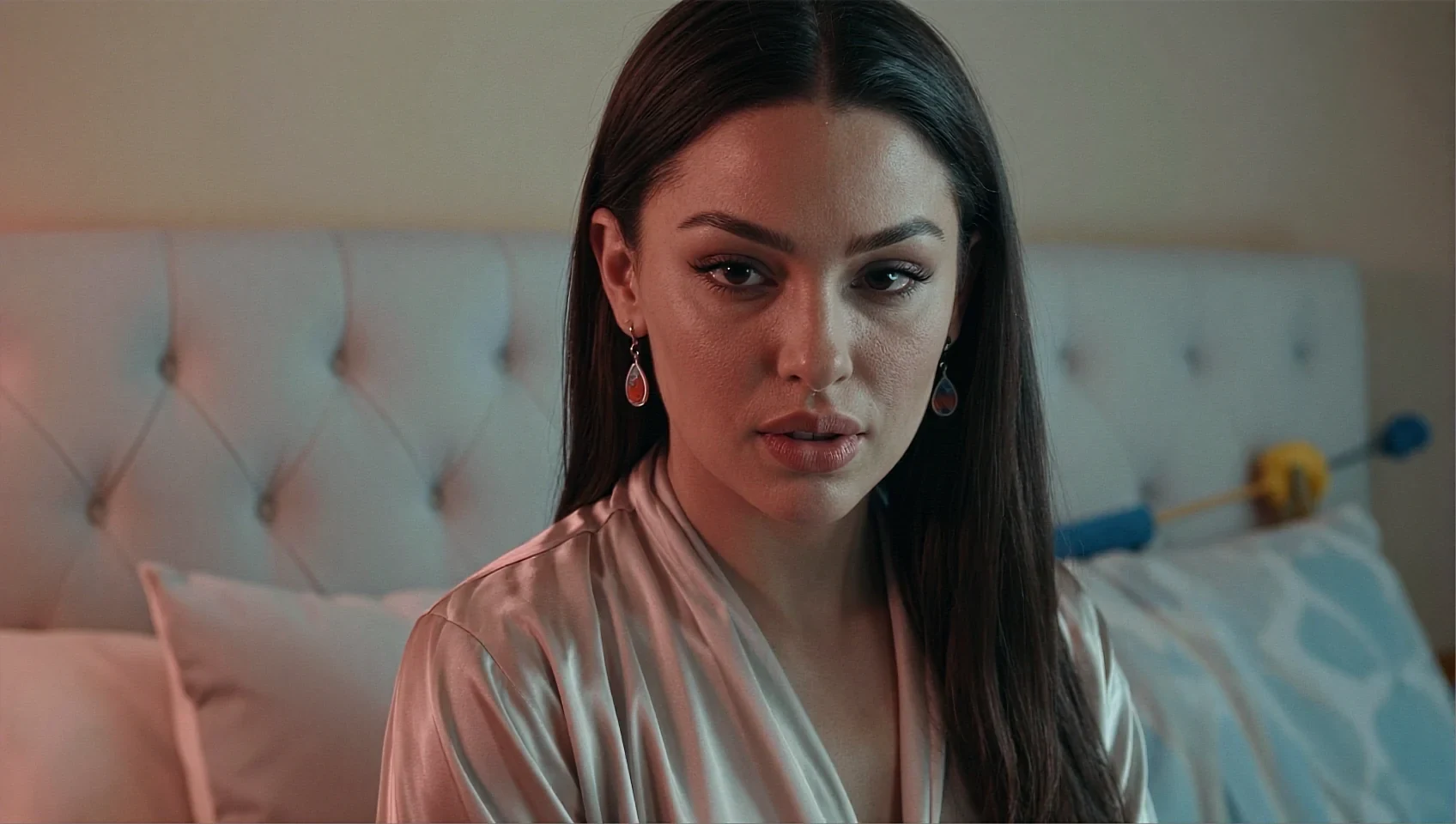 Wide shot of a fictional AI character in a peach satin robe, sitting up against a padded headboard